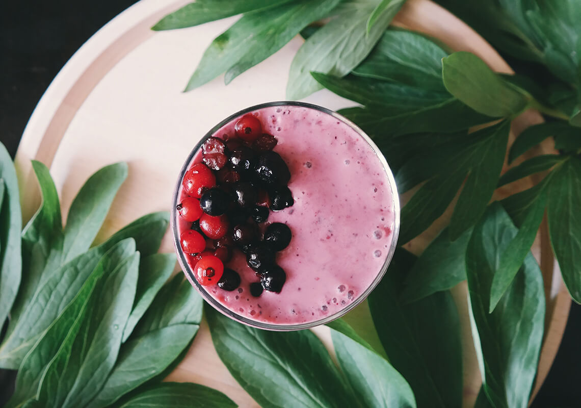 pink berry smoothie on plate surrounded by green leaves