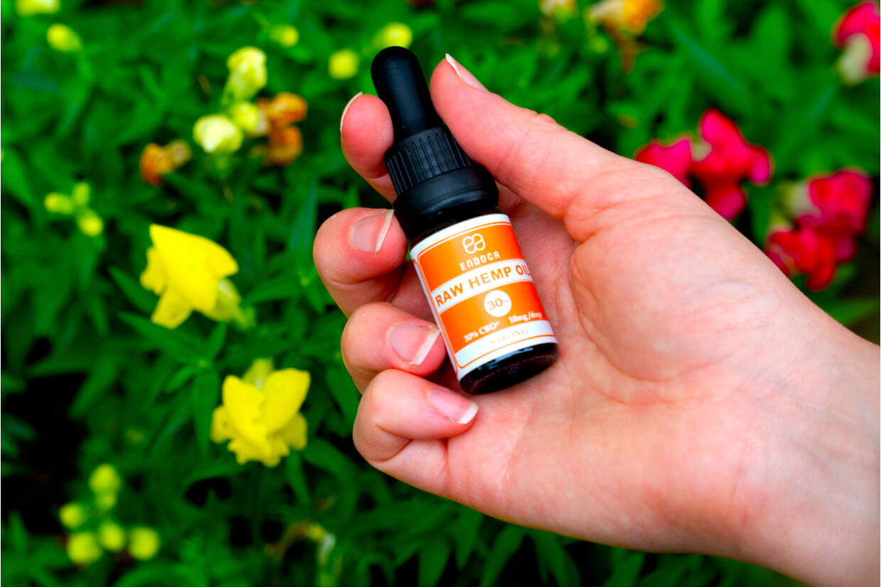 Hand holding CBD drops above flowers in nature