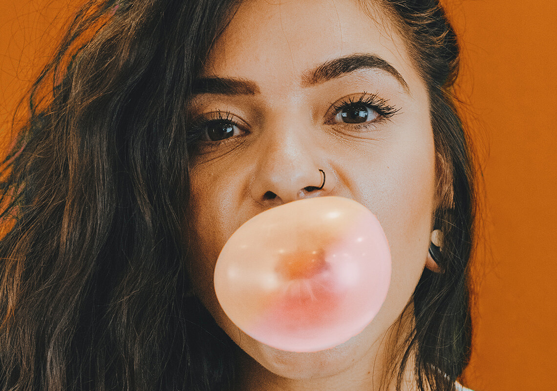 Girl blowing a bubble with her gum in front of orange background