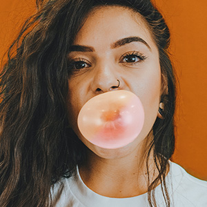 Girl blowing a bubble with her gum in front of orange background