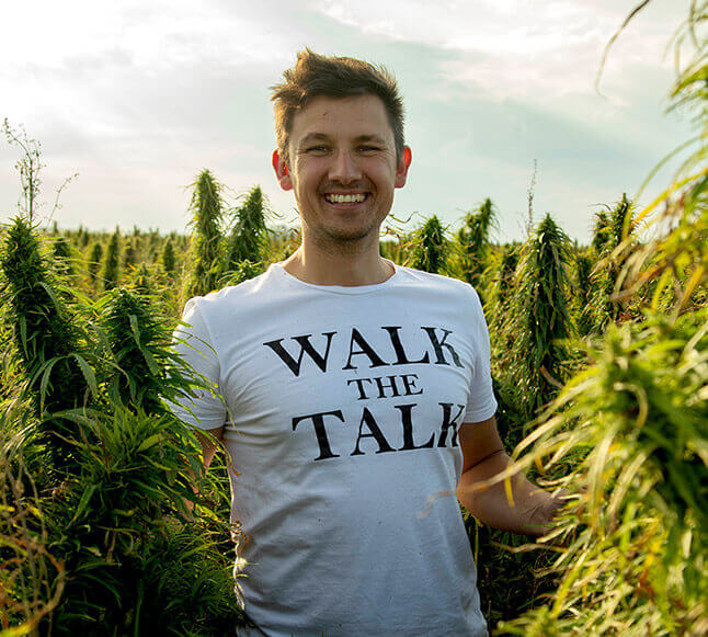 Man in hemp field wearing white t-shirt with words ‘walk the talk’