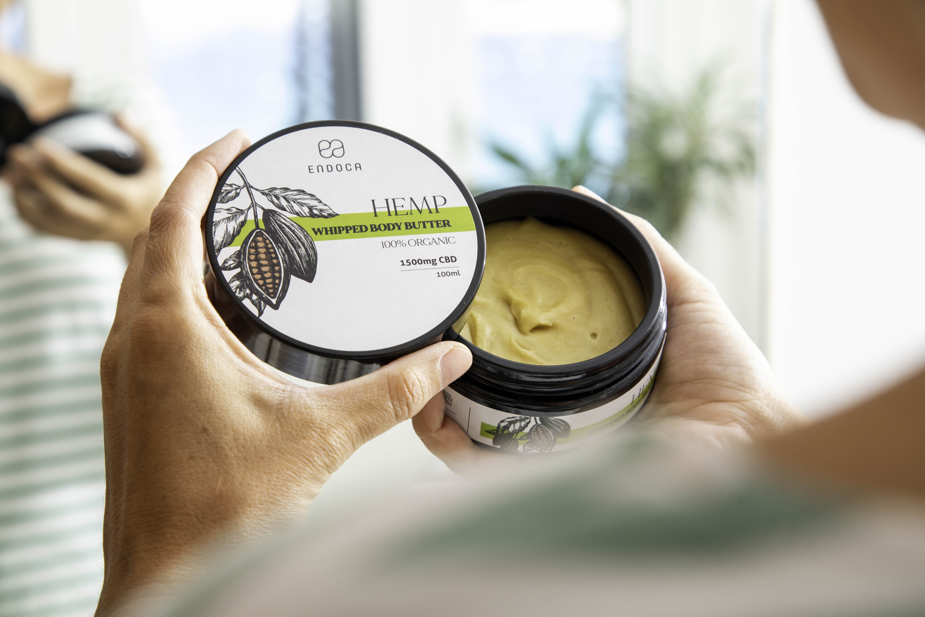 Hand holding an open tin of Endoca hemp whipped body butter
