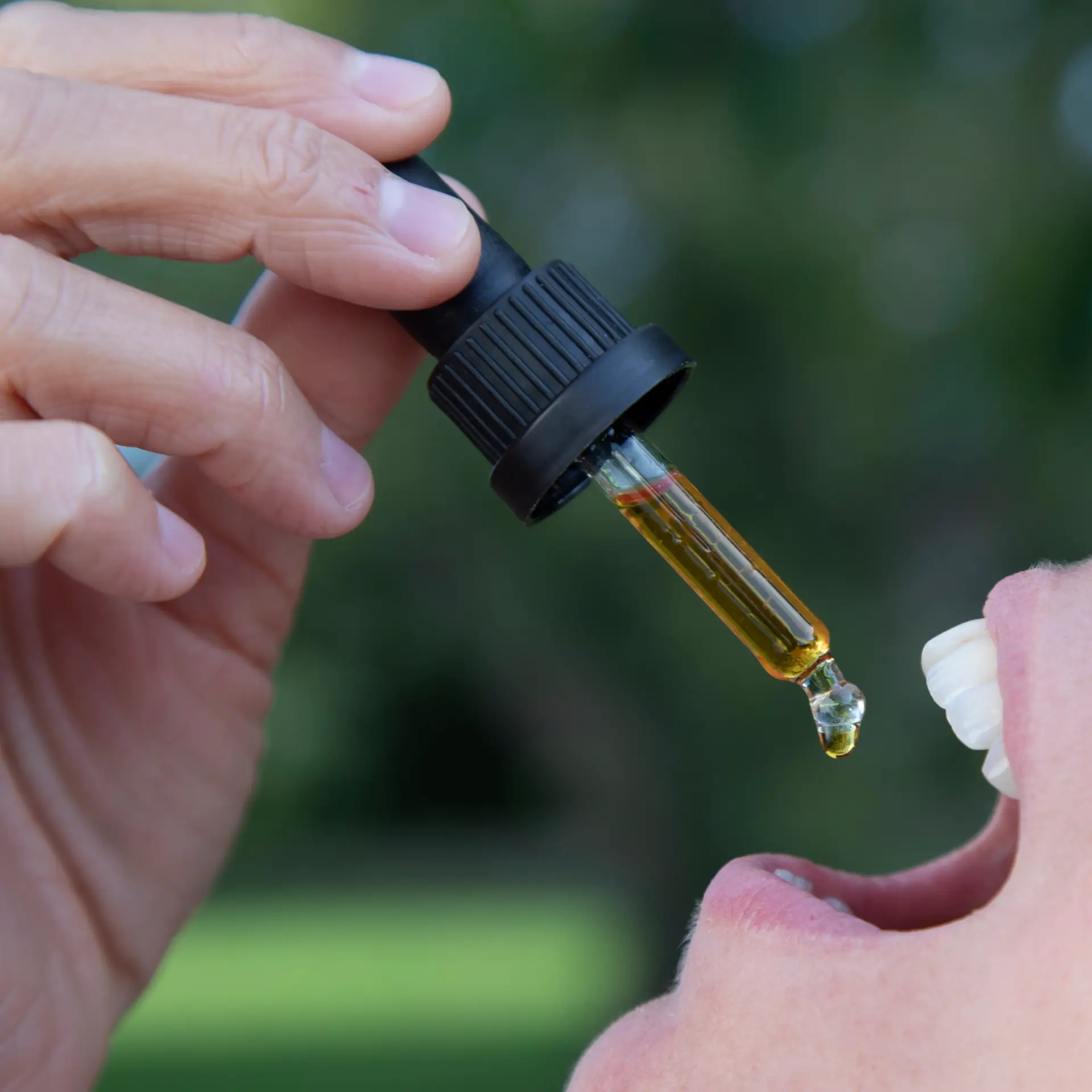 Golden CBD oil dosed from a glass dropper onto the tongue, close-up