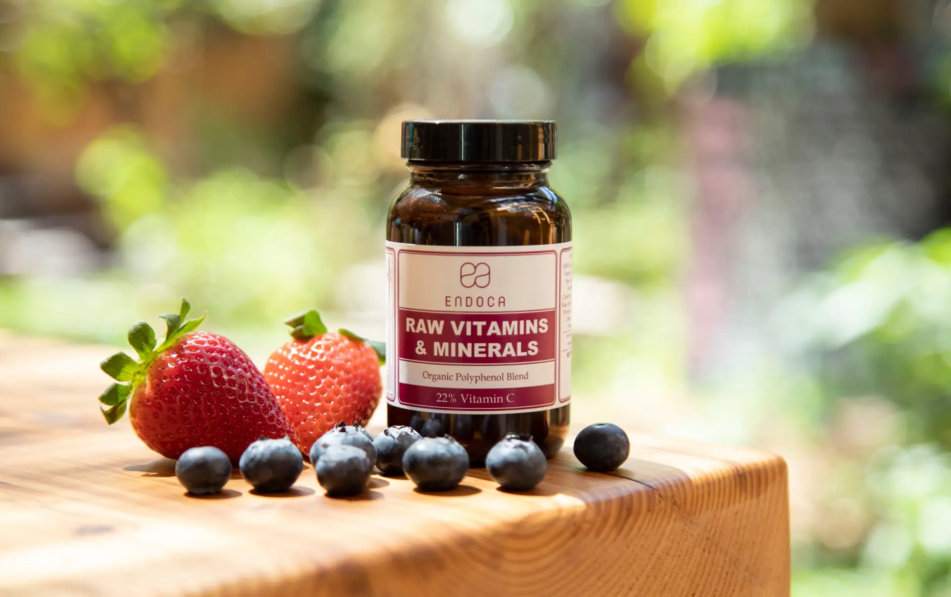Endoca Raw Vitamins and Minerals bottle on a wooden ledge with fresh strawberries and blueberries