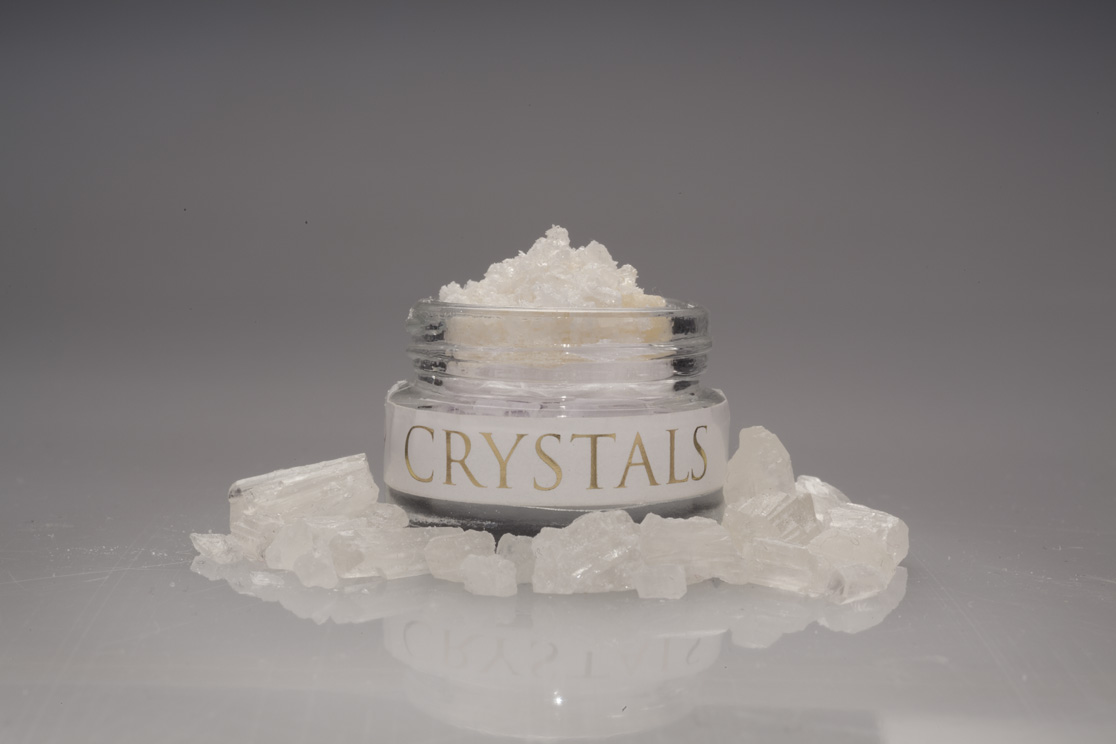 Jar of pure CBD crystals surrounded by CBD isolate chunks on a dark background